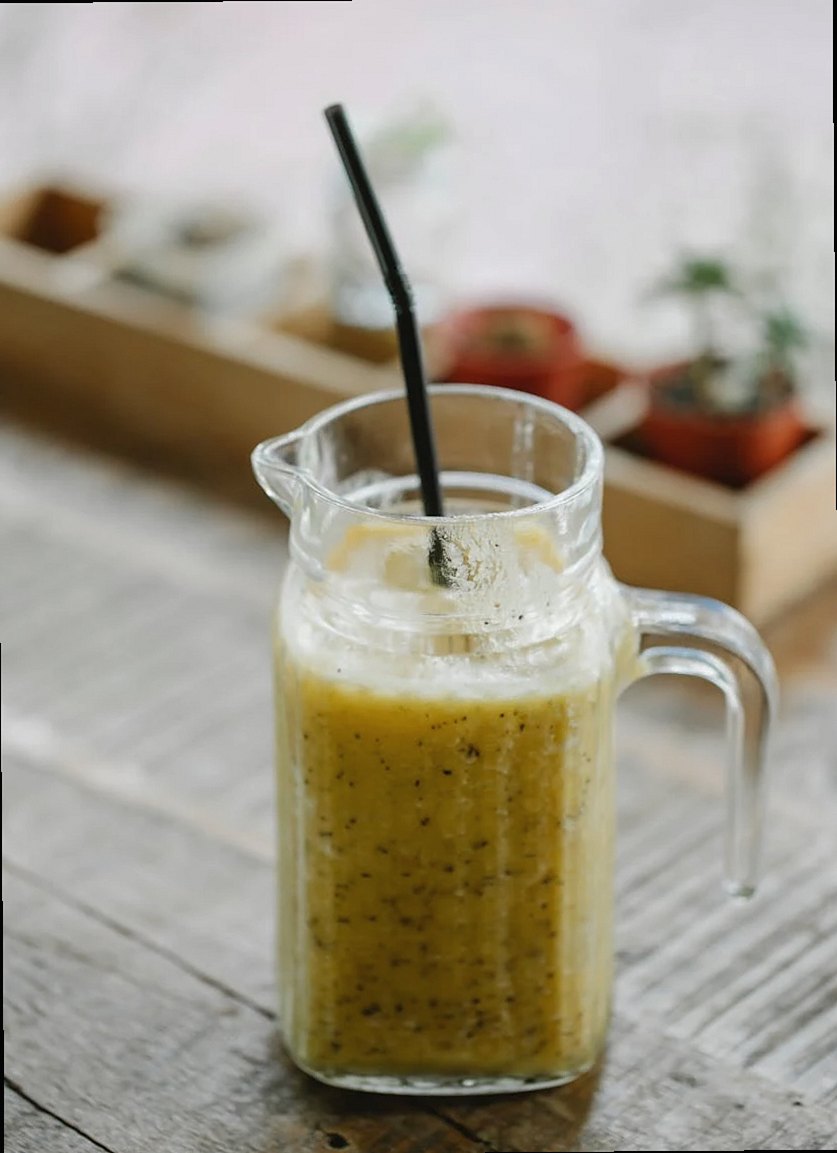 Jarra con batido de plátano fresco y saludable con pajita servida en mesa de madera a la luz del día